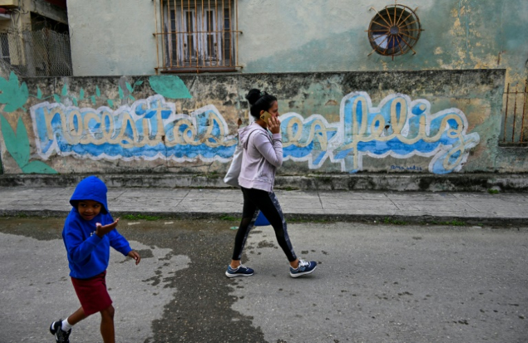 Des Cubains marchent devant le graffiti "Necesitas ser feliz" (Tu dois être heureux) du graffeur cubain Mr. Sad, à La Havane, le 12 décembre 2024 ( AFP / YAMIL LAGE )