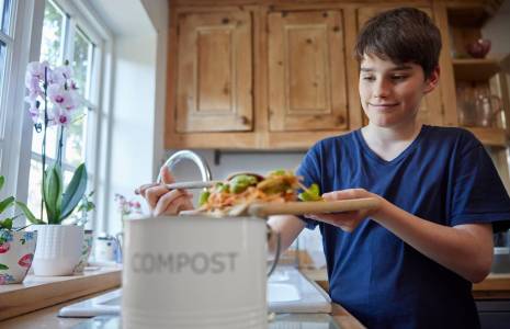 (Crédits photo : Adobe Stock - Adolescent remplissant un seau de compost avec des épluchures de légumes dans sa cuisine)