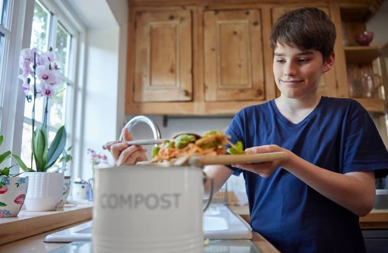 (Crédits photo : Adobe Stock - Adolescent remplissant un seau de compost avec des épluchures de légumes dans sa cuisine)