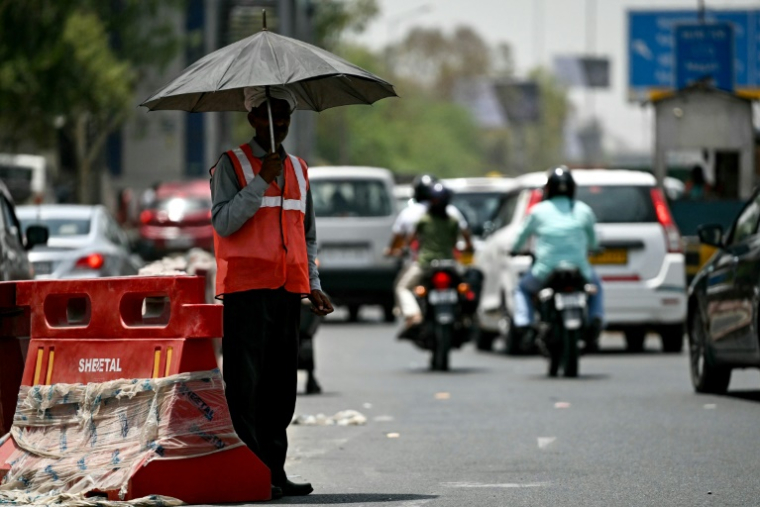 Un employé fait la navette protégé par un parapluie dans la chaleur à New Delhi, en Inde, le 29 mai 2024 (AFP / Arun SANKAR)