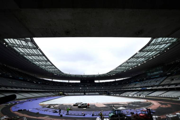 Des ouvriers posent des pistes d'athlétisme violettes pendant les travaux de rénovation pour adapter le Stade de France en vue des Jeux olympiques de Paris 2024, à Saint-Denis, en banlieue parisienne, le 9 avril 2024 ( AFP / Anne-Christine POUJOULAT )