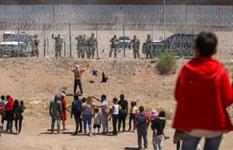 Des migrants cherchant à entrer aux Etats-Unis devant une barrière de fil barbelé et des agents de la Garde nationale du Texas, à la frontière entre le Mexique et les Etats-Unis, à Ciudad Juarez, le 13 mai 2024 ( AFP / HERIKA MARTINEZ )