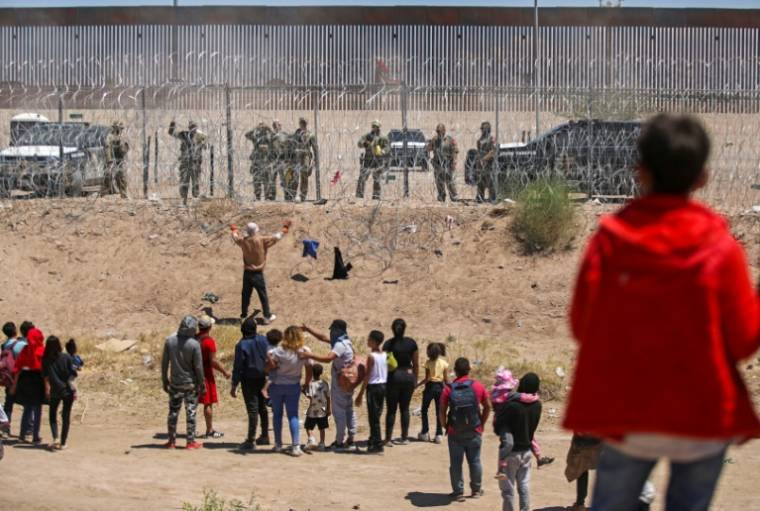 Des migrants cherchant à entrer aux Etats-Unis devant une barrière de fil barbelé et des agents de la Garde nationale du Texas, à la frontière entre le Mexique et les Etats-Unis, à Ciudad Juarez, le 13 mai 2024 ( AFP / HERIKA MARTINEZ )
