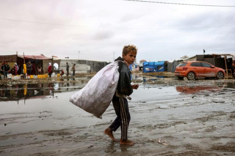 Un enfant palestinien déplacé portant un sac marche pieds nus dans un camp inondé, suite à de fortes pluies au nord de Deir el-Balah dans le centre de la bande de Gaza, le 24 novembre 2024 ( AFP / Bashar TALEB )