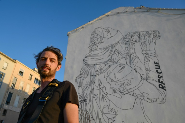 Le street-artist Mahn Kloix devant sa fresque géante créée en hommage aux sauveteurs du navire-ambulance SOS Méditerranée sur le "mur Zidane" à Marseille, le 31 octobre 2024 ( AFP / Christophe SIMON )