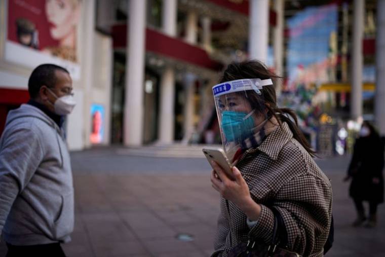 Une femme portant un masque de protection et un écran facial marche à Shanghai, en Chine