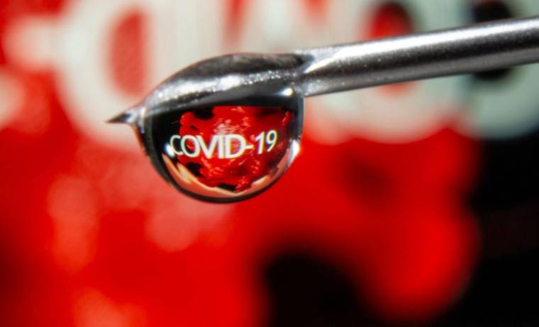 Le mot "COVID-19" se reflète dans une goutte sur une aiguille de seringue