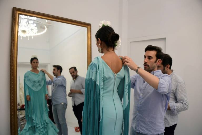 Le couturier espagnol Luis Fernández (c) ajuste une robe de flamenco sur sa cliente Virginia Cuaresma, dans son atelier de Séville, le 8 avril 2024 ( AFP / CRISTINA QUICLER )