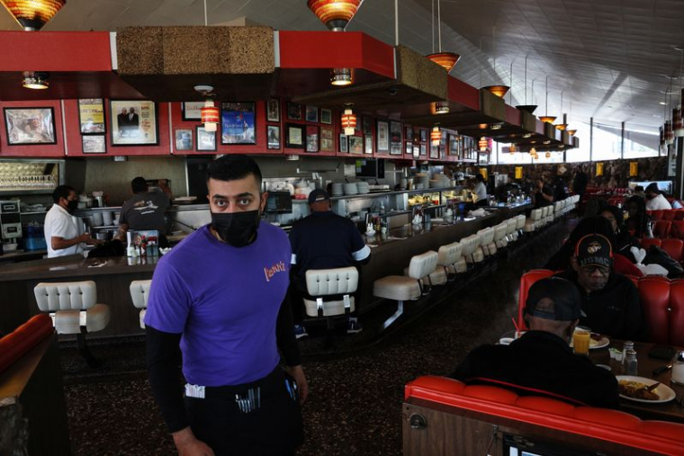 Un serveur portant un masque de protection passe devant des clients qui mangent chez Pann's, un café classique des années 1950, à Los Angeles