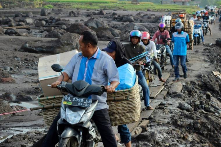 Des habitants roulent à moto sur un sentier de fortune fait de dalles de bois pour éviter la boue causée par des inondations dans le village de Rambatan, sur l'île indonésienne de Sumatra, le 14 mai 2024 ( AFP / ADE YUANDHA )