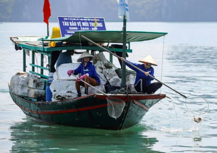 Des travailleurs ramassent à l'épuisette des déchets dans la baie d'Ha Long, au Vietnam, le 17 mai 2023 ( AFP / Nam NGUYEN )
