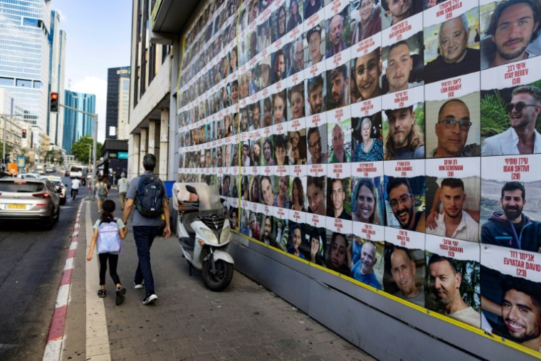 Des personnes passent devant des affiches des otages emmenés dans la bande de Gaza lors de l'attaque du Hamas le 7 octobre, à Tel-Aviv, le 11 août 2024 ( AFP / Oren ZIV )