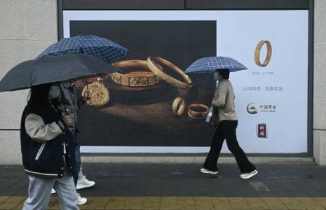 Des passants avec des parapluies marchent devant un panneau publicitaire à Pékin le 10 avril 2024 ( AFP / WANG Zhao )