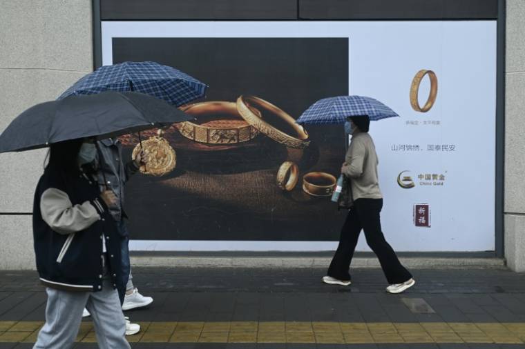 Des passants avec des parapluies marchent devant un panneau publicitaire à Pékin le 10 avril 2024 ( AFP / WANG Zhao )