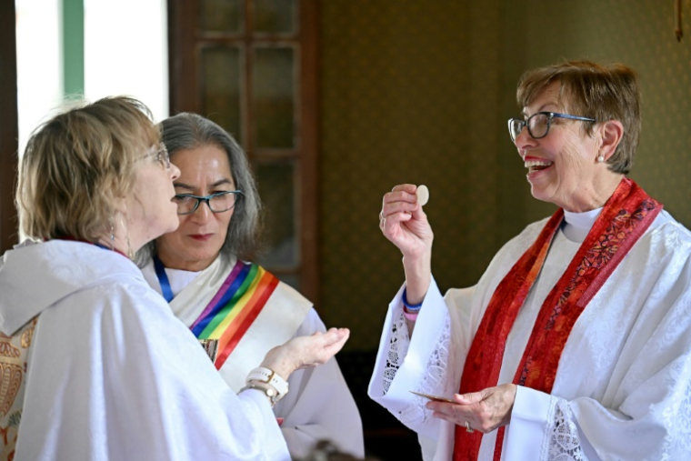 Newly-ordinated "priest" Mary Katherine Daniels and newly-ordinated "diaconate" Maria Teresa Ribeiro Rosa take part in a secrete ordinations of women ceremony on a barge on the river Tiber in Rome, on October 17, 2024. With bible readings, hymns, etc, the three-language ceremony, organized with the utmost discretion in the presence of some 50 faithful from several countries, followed the same liturgy as an official mass. Yet it is illegal in the eyes of the Church, as according to canon law, it even earns the six ordained - three priests and three deacons, including five women and one transgender man - and each participant automatic excommunication. ( AFP / Filippo MONTEFORTE )