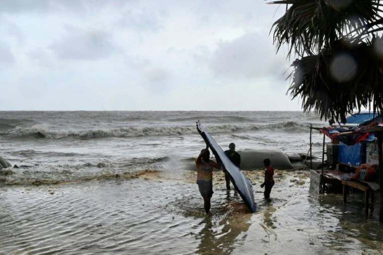 Des hommes transportent leur atelier de fortune au bord de la mer à titre préventif lors des pluies à Kuakata le 26 mai 2024, avant l'arrivée dimanche soir du cyclone Remal au Bangladesh.  ( AFP / Munir UZ ZAMAN )