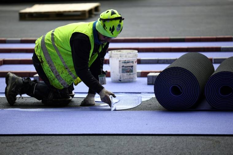 Un ouvrier pose des pistes d'athlétisme violettes pendant les travaux de rénovation pour adapter le Stade de France en vue des Jeux olympiques de Paris 2024, à Saint-Denis, en banlieue parisienne, le 9 avril 2024 ( AFP / Anne-Christine POUJOULAT )