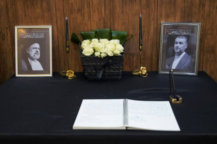 Un livre de condoléances devant les portraits du président iranien Ebrahim Raïssi (g) et du ministre iranien des Affaires étrangères Hossein Amir-Abdollahian (d) au consulat de la république islamique à Najaf, le 20 mai 2024 en Irak ( AFP / Qassem al-KAABI )