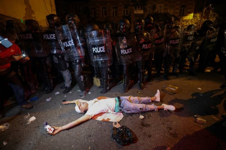 Un manifestant s'allonge sur le sol devant des agents de police, le 30 avril 2024 à Tbilissi ( AFP / Giorgi ARJEVANIDZE )
