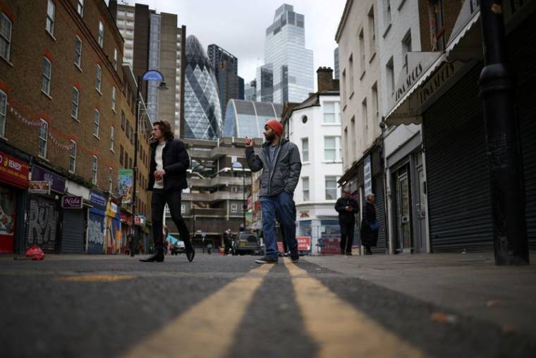 Des personnes passent devant des magasins, avec le quartier financier de la City de Londres en arrière-plan