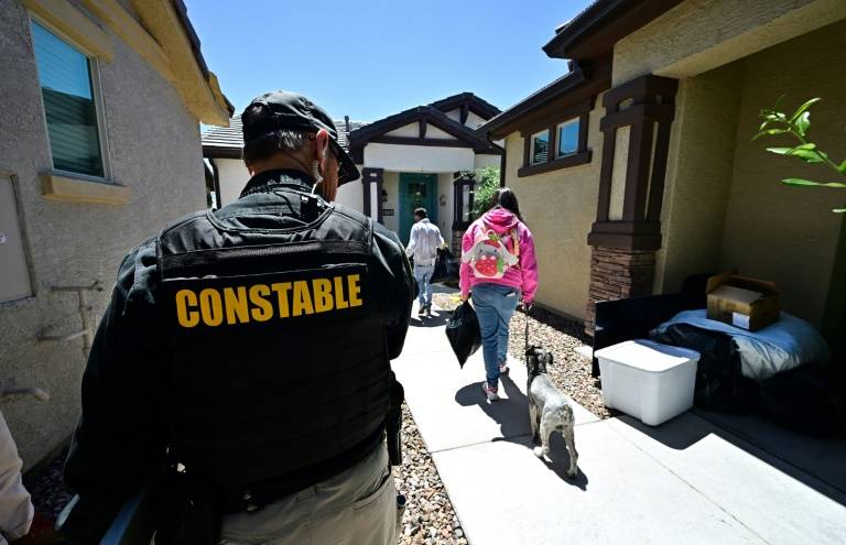 Lennie McCloskey, agent de police de la circonscription judiciaire de Manistee, dans le comté de Maricopa, observe une famille qui vient d'être expulsée, à Phoenix (Arizona), aux Etats-Unis, le 15 avril 2024 ( AFP / Frederic J. BROWN )