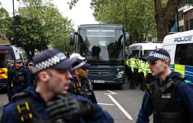 Des policiers escortent, lors d'une manifestation, un bus qui conduirait des migrants et des demandeurs d'asile d'un hôtel de Peckham, au sud de Londres, vers la barge Bibby Stockholm à Portland, dans le Dorset, au sud-ouest de l'Angleterre, le 2 mai 2024 ( AFP / HENRY NICHOLLS )