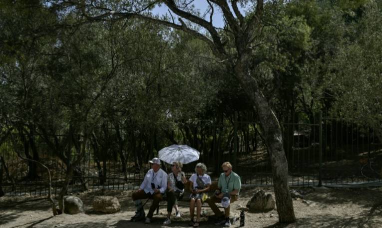 Des touristes sont assis à l'ombre près de l'Acropole à Athènes pendant une journée de canicule, le 12 juin 2024 ( AFP / STRINGER )