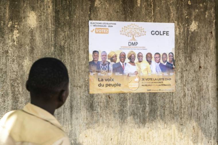 Un homme regarde une affiche électorale de la Dynamique pour la majorité du peuple (DMP), regroupement au Togo de partis politiques de l’opposition et d’organisations de la société civile, à Lomé le 24 avril 2024 ( AFP / Dodo ADOGLI )