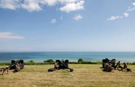 Des militaires américains se rassemblent près de canons d'artillerie de campagne surplombant la plage d'Omaha et la Manche, près du cimetière américain de Colleville-sur-Mer, dans le nord-ouest de la France, le 5 juin 2024 ( AFP / Ludovic MARIN )