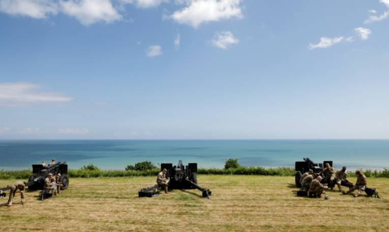 Des militaires américains se rassemblent près de canons d'artillerie de campagne surplombant la plage d'Omaha et la Manche, près du cimetière américain de Colleville-sur-Mer, dans le nord-ouest de la France, le 5 juin 2024 ( AFP / Ludovic MARIN )