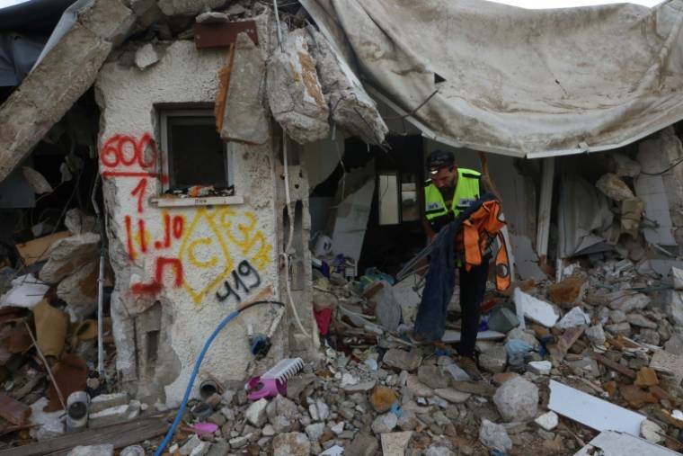Un membre de l'équipe d'intervention d'urgence juive ultra-orthodoxe israélienne Zaka récupère des objets et vêtements dans les décombres d'une maison dans le kibboutz Kfar Aza, près de la frontière avec la bande de Gaza, le 14 novembre 2023 ( AFP / GIL COHEN-MAGEN )