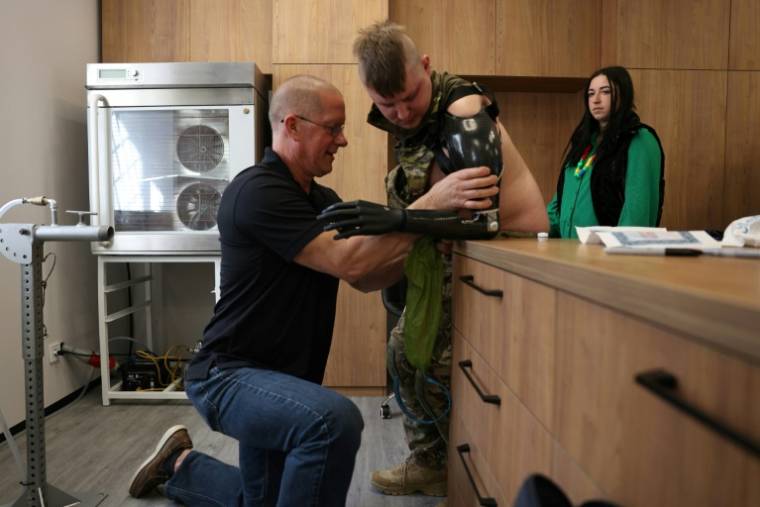 Le prothésiste James Allan ajuste une prothèse de main bionique sur l'avant-bras du sergent ukrainien Valeriï Koutcherenko, en présence de sa femme Veronika, dans les locaux de l'ONG américaine Protez Foundation à Kiev, le 2 avril 2024 ( AFP / Anatolii STEPANOV )