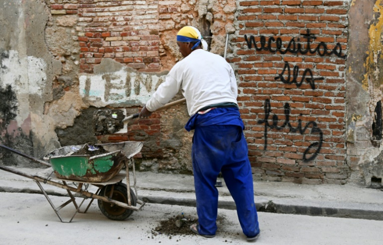 Un homme travaille près d'un mur portant le graffiti "Necesitas ser feliz" (Tu dois être heureux) du graffeur cubain Mr. Sad à La Havane, le 12 décembre 2024 ( AFP / YAMIL LAGE )