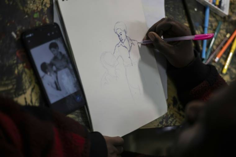 Un artiste du collectif "Art for Memories" dessine le portrait de victimes du génocide rwandais à partir d'une photo, le 2 avril 2024 à Kigali ( AFP / Guillem Sartorio )