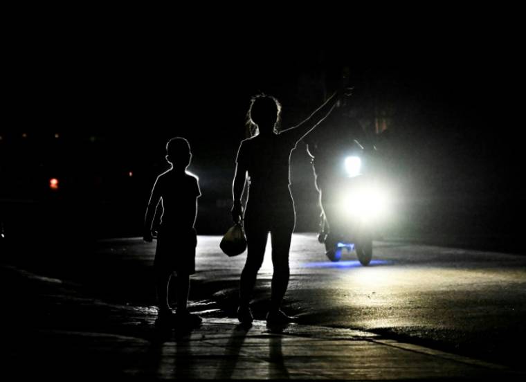Une femme avec son fils dans une rue plongée dans l'obscurité, lors d'une coupure de courant à Bauta, le 18 mars 2024 dans la province d'Artemisa, à Cuba ( AFP / YAMIL LAGE )