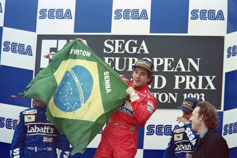Ayrton Senna, alors pilote chez McLaren, brandit le drapeau brésilien sur le podium du Grand Prix d'Europe, le 11 avril 1993 à Donington (Royaume-Uni) ( AFP / Pascal PAVANI )