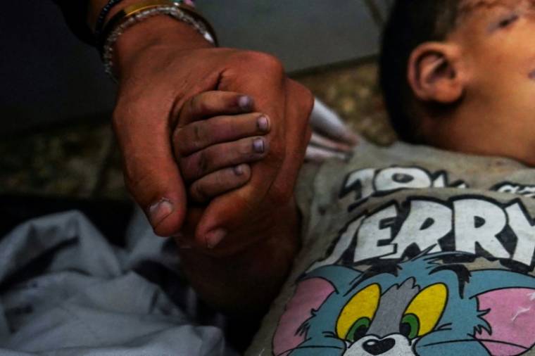 Un homme tenant la main d'un garçon tué lors d'un bombardement pleure à l'hôpital Al-Aqsa à Nousseirat, dans la bande de Gaza, le 27 mai 2024 ( AFP / Bashar TALEB )