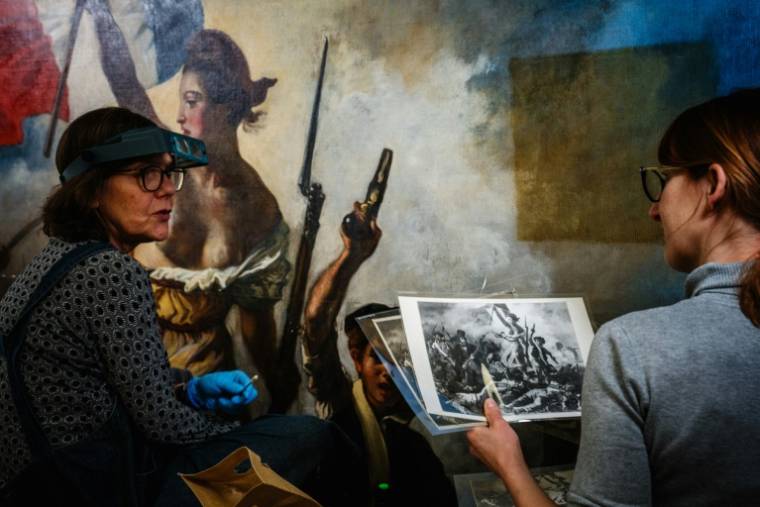 Des restaurateurs travaillent sur le tableau "La liberté guidant le peuple" d'Eugène Delacroix, dans un laboratoire du Musée du Louvre à Paris, le 28 février 2024 ( AFP / Dimitar DILKOFF )