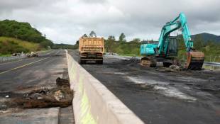 Des engins de chantier enlèvent des débris sur la route RT1 qui mène à l'aéroport international de Nouméa, le 19 mai 2024 ( AFP / Delphine Mayeur )