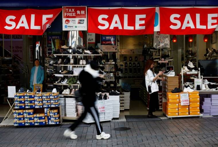 Un passant passe devant un magasin de détail affichant des bannières "SALE" à Tokyo