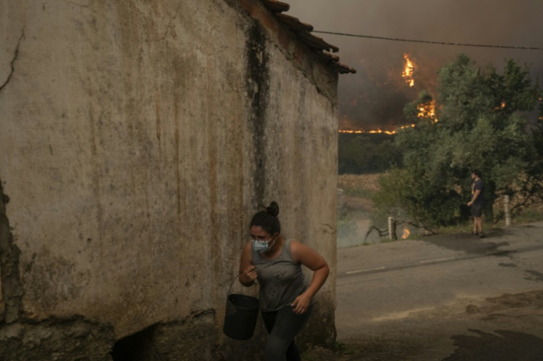 Une femme porte un seau d'eau alors qu'un incendie fait rage à Busturenga, dans la région d'Aveiro, dans le nord du Portugal, le 16 septembre 2024 ( AFP / Patricia DE MELO MOREIRA )