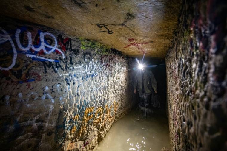 Un cataphile, lampe frontale sur la tête, avance les pieds dans l'eau dans les carrières souterraines de Paris, le 20 avril 2024  ( AFP / MIGUEL MEDINA )