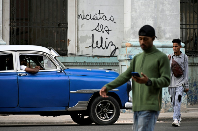 Des Cubains marchent devant le graffiti "Necesitas ser feliz" (Tu dois être heureux) du graffeur cubain Mr. Sad, à La Havane, le 12 décembre 2024 ( AFP / YAMIL LAGE )