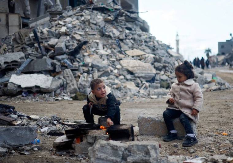Des enfants palestiniens sont assis près du feu, à côté des décombres d'une maison, à Khan Younis