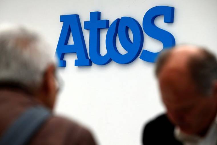 Des personnes marchent devant le logo de la société Atos à Paris, en France