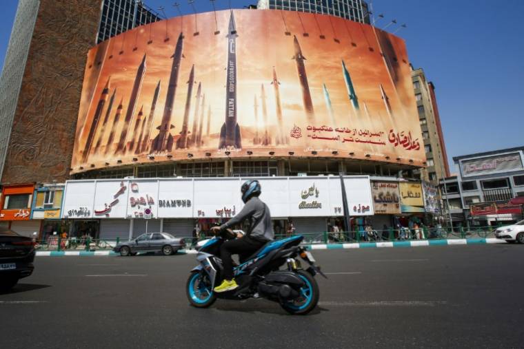 Un homme passe en moto devant un panneau d'affichage représentant des missiles balistiques iraniens en service à Téhéran, le 19 avril 2024. ( AFP / - )
