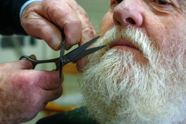 Le coiffeur Roger Amilhastre (G), âgé de 90 ans, taille la barbe d'un client dans son salon à Saint-Girons, en Ariège, le 16 avril 2024  ( AFP / Ed JONES )