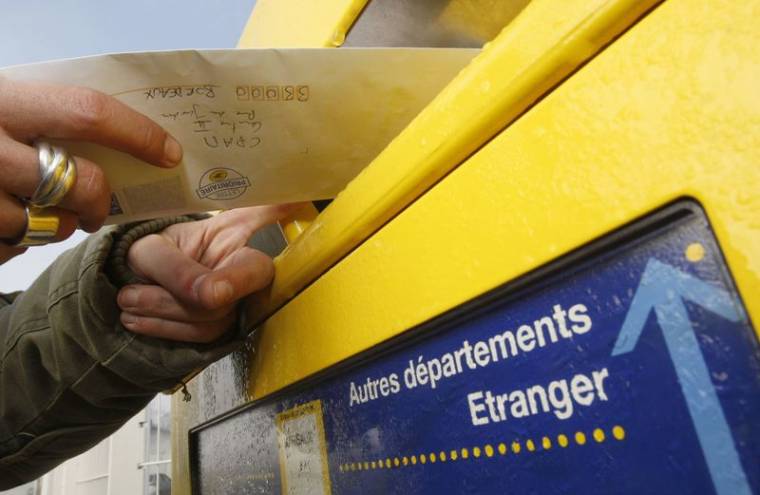 Un homme poste une lettre dans la boîte aux lettres de La Poste à Margaux