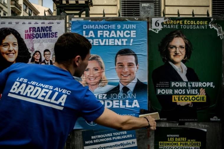 Un bénévole du RN colle une affiche de campagne de Jordan Bardella, président du parti et tête de liste aux européennes, le 6 mai 2024 à Lyon ( AFP / JEFF PACHOUD )