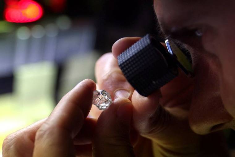 Un employé examine un diamant brut à l'usine "Flanders Manufacturing"